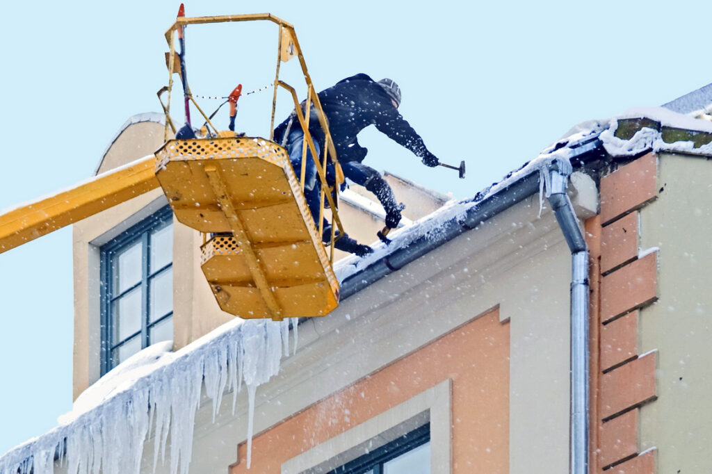 Workers clean snow and icicle from a house roof